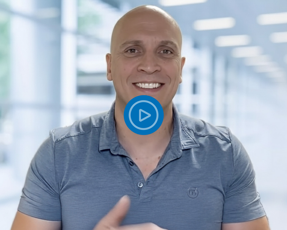 Man in a gray polo shirt with a blue play button icon over his chest, set against a blurred indoor background.