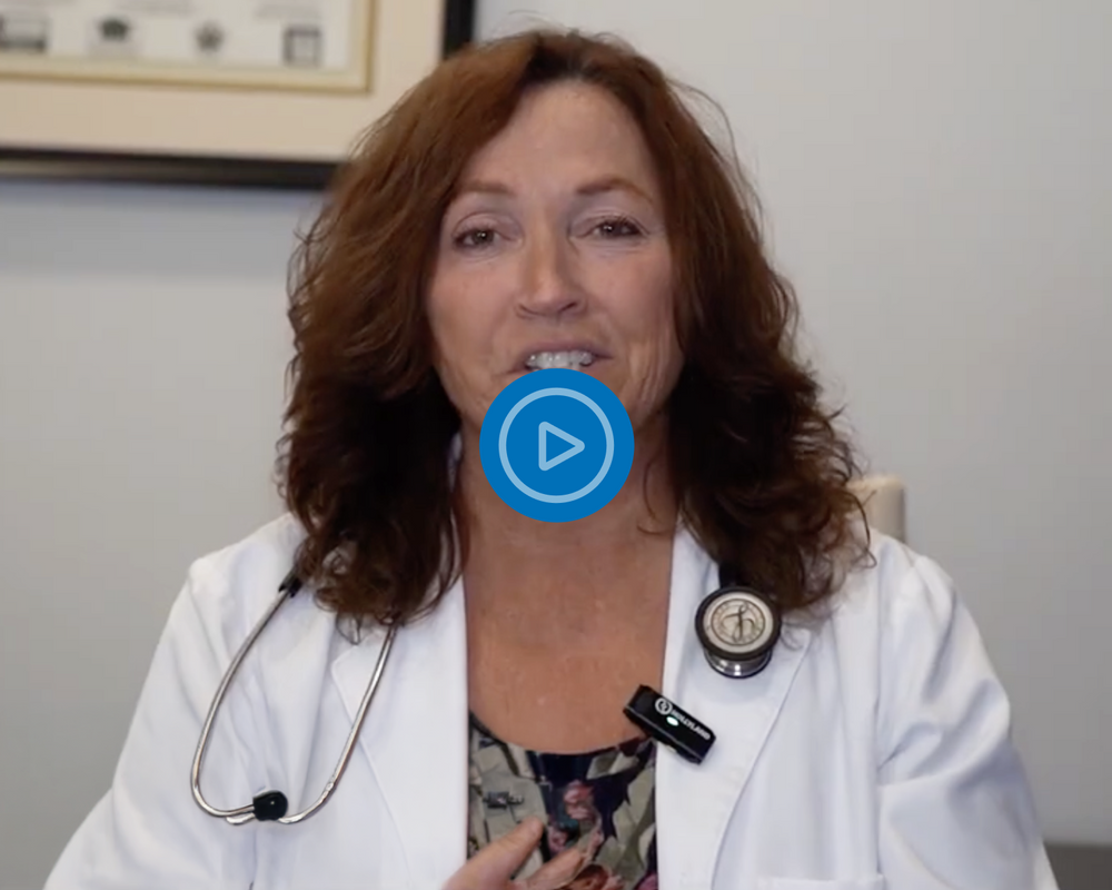 Woman in a white coat with a stethoscope, likely a doctor, in an indoor setting.